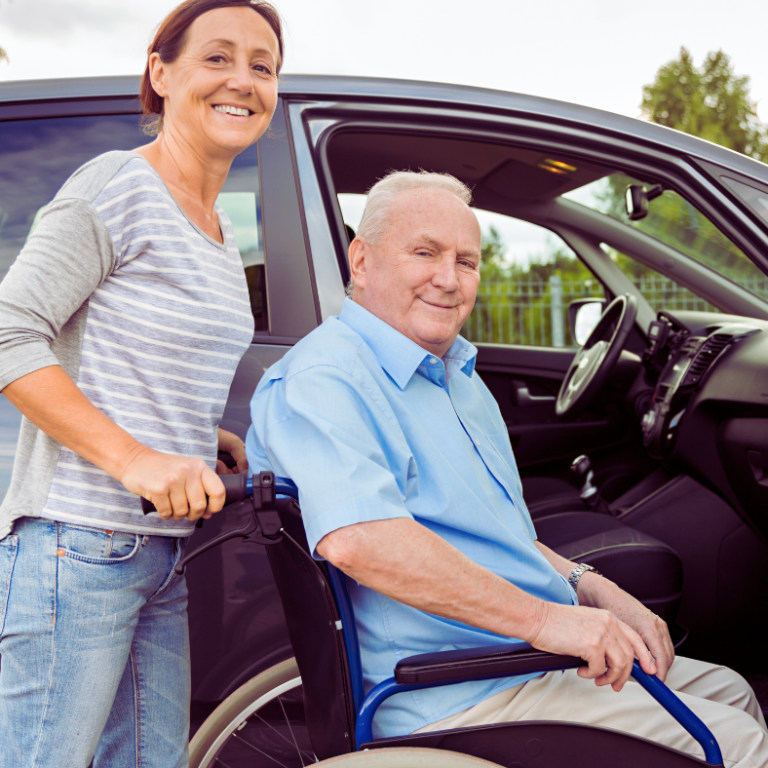 Woman assisting an elderly man in a wheelchair by a parked car.