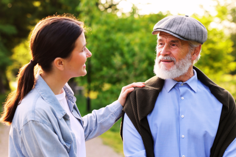 A young woman converses with an elderly man in a serene, green outdoor setting.