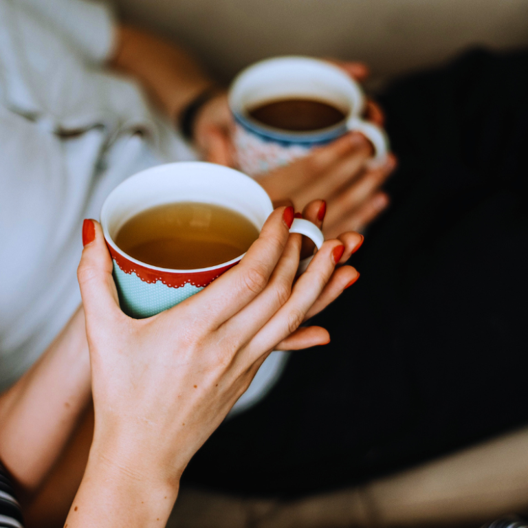 Two people holding colourful mugs of tea or coffee, sitting together.